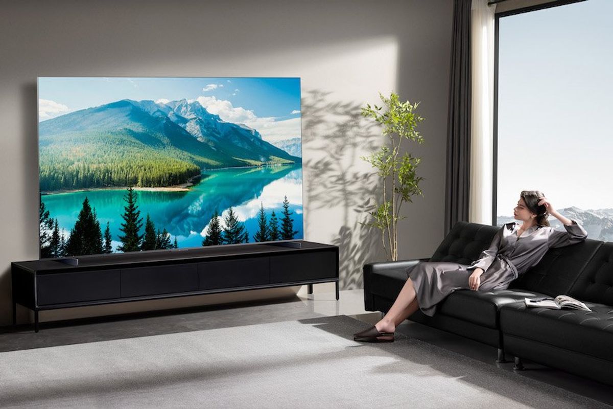 Photo of TCL AM8K Smart TV on a entertainment center in a room with a woman sitting on the couch watching tv